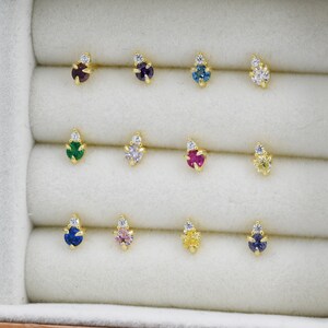 May include: A set of 10 pairs of small gold stud earrings with a single gemstone and a small diamond accent. The gemstones are in various colors, including green, blue, pink, red, and yellow.