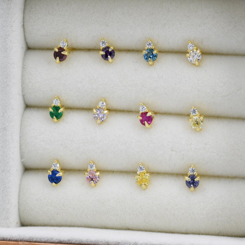 May include: A set of 10 pairs of small gold stud earrings with a single gemstone and a small diamond accent. The gemstones are in various colors, including green, blue, pink, red, and yellow.