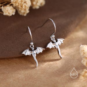 May include: A pair of silver dragon dangle earrings. The dragons are facing forward with their wings spread out.