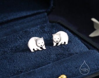 May include: A pair of silver earrings featuring a small, detailed wombat design. The earrings are displayed in a blue velvet jewelry box.