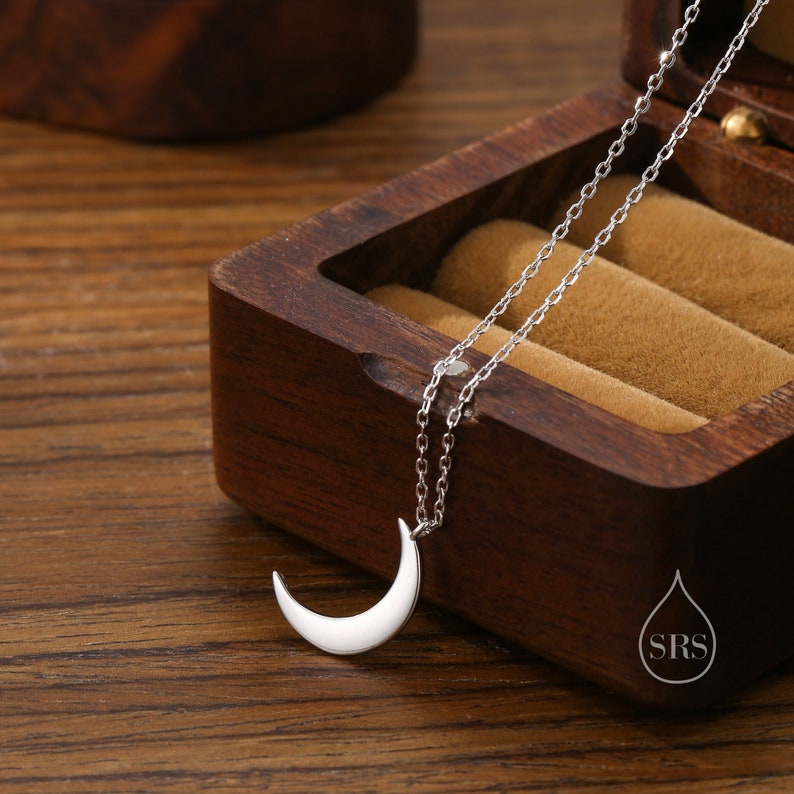 May include: A silver crescent moon pendant necklace on a silver chain. The necklace is displayed in a wooden box.