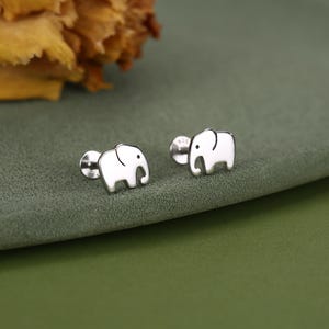 May include: A pair of silver-toned stud earrings shaped like small elephants. Each earring features a smooth, polished surface with a simple etched line to define the elephant's ear and a small black dot for the eye, attached to a flat circular post back.