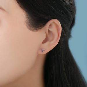 Puede incluir: Primer plano de la oreja de una persona con un peque&ntilde;o pendiente de lazo plateado.