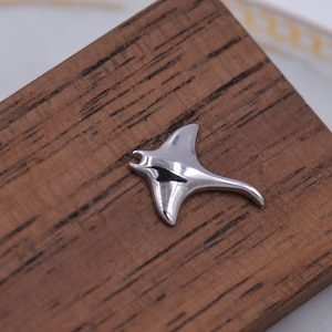 May include: A silver-colored manta ray charm, made of metal, on a wooden surface.