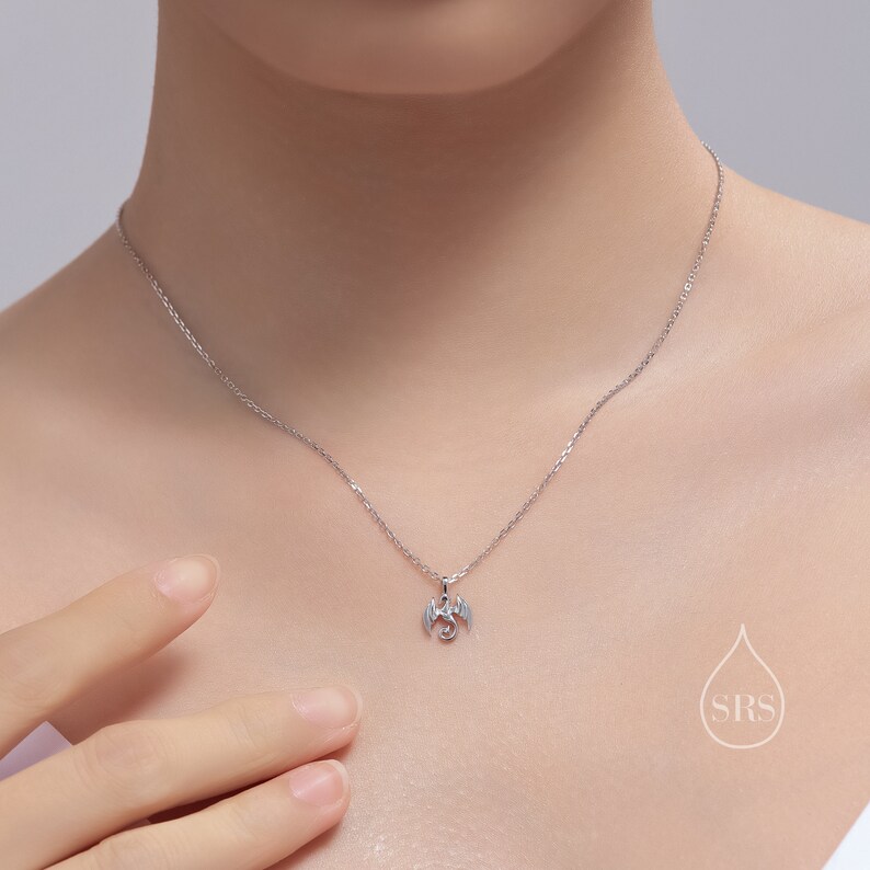 May include: A silver necklace with a small dragon pendant. The dragon is facing to the right with its wings spread out.