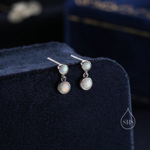 Puede incluir: Un par de pendientes de plata con dos piedras de ópalo blanco en cada pendiente. Los pendientes son colgantes y tienen un diseño sencillo.
