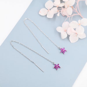 Puede incluir: Un par de pendientes de cadena de plata con colgantes de flores rosas. Los pendientes tienen un diseño delicado de cadena y son perfectos para agregar un toque de elegancia a cualquier atuendo.
