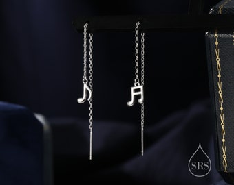 May include: A pair of silver dangle earrings with a music note charm. The earrings are on a black background.