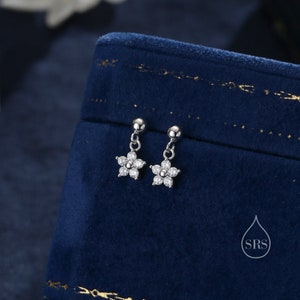 May include: A pair of silver dangle earrings with a small flower charm. Each flower charm is made of clear cubic zirconia stones.