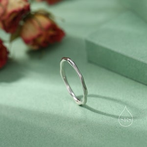 May include: A silver ring with a wavy, organic design. The ring is on a green surface.