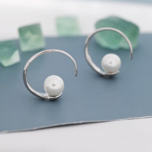 Op de afbeelding: Een paar zilveren oorringen met een enkele witte parel op elke ring.