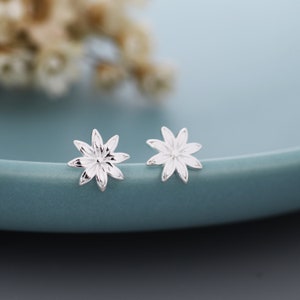 May include: A pair of silver flower-shaped stud earrings. The earrings are small and delicate, with a simple design.