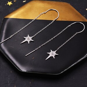 May include: A pair of silver dangle earrings with a star-shaped charm. Each earring has a small clear stone in the center of the star.