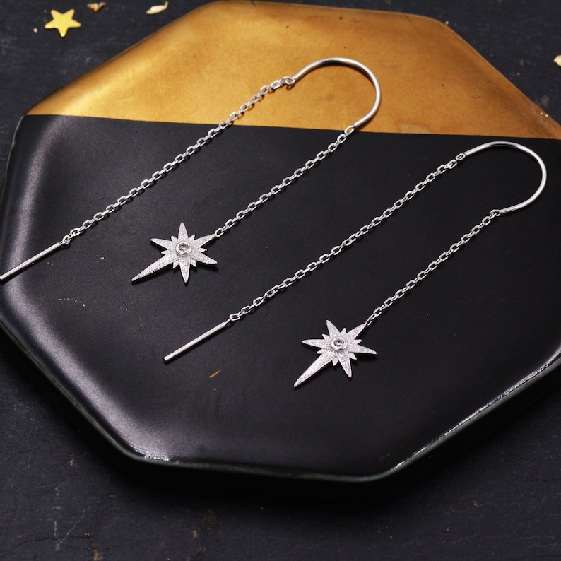 May include: A pair of silver dangle earrings with a star-shaped charm. Each earring has a small clear stone in the center of the star.
