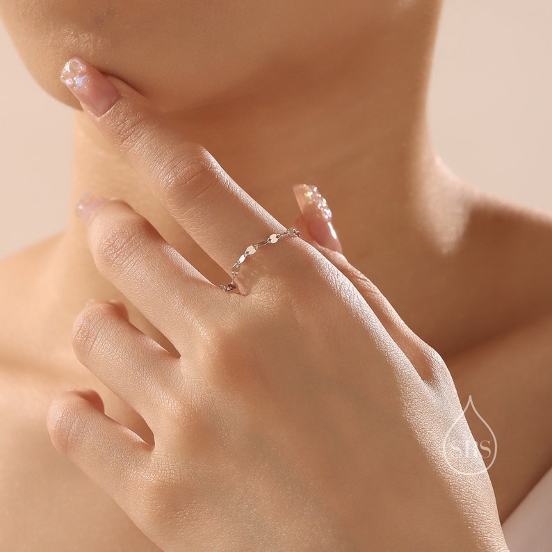 May include: A delicate silver ring with a chain design featuring small, round, and slightly textured links.