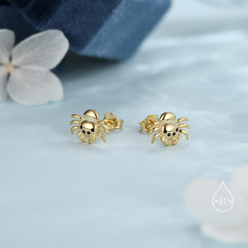 May include: A pair of gold spider stud earrings. The spiders have black eyes and are set on a post with a butterfly back.