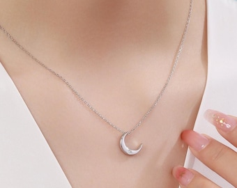May include: A silver-toned necklace featuring a delicate crescent moon pendant. The pendant is suspended from a thin, matching silver-toned chain and includes a single small, clear, sparkling stone embedded near the tip of the moon shape.