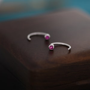 May include: A pair of silver hoop earrings with a small pink gemstone on each hoop.