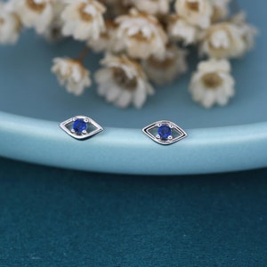 May include: A pair of silver earrings with a blue evil eye design. The earrings are small and delicate.