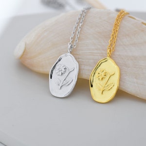 May include: Two delicate necklaces with oval pendants featuring a raised flower design. One necklace has a silver pendant and the other has a gold pendant.