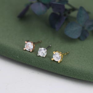 Op de afbeelding: Drie oorknopjes met ronde, heldere, gefacetteerde stenen in vier-poot metalen zettingen. De oorbellen zijn afgewerkt in drie verschillende metaaltinten: roségoud, zilver en geelgoud, elk voorzien van een steker voor een veilige bevestiging.