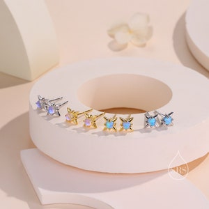 Puede incluir: Un conjunto de cuatro pares de pendientes de estrella plateados y dorados con piedras de ópalo azul iridiscente.