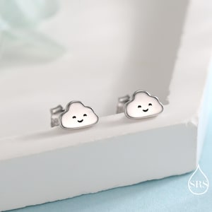 May include: A pair of silver cloud-shaped stud earrings. Each earring features a white cloud with a smiling face and a silver border. The earrings are displayed on a white surface.