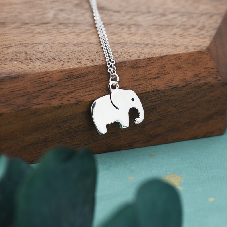 May include: A silver necklace with a small elephant charm. The elephant is facing to the right and has a simple design.