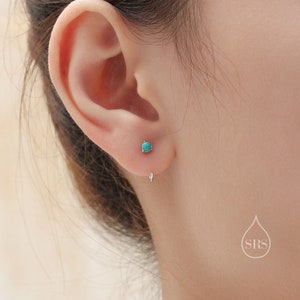 以下が含まれることがあります： 小さなターコイズスタッドピアスをつけた耳のクローズアップ。ピアスはシルバーメタルにセットされています。2つ目のシルバーのイヤリングバックが耳たぶの下に見えます。背景は柔らかくニュートラルな色調です。