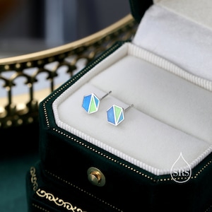 May include: A pair of silver hexagonal stud earrings with blue and green enamel. The earrings are in a green velvet jewellery box.