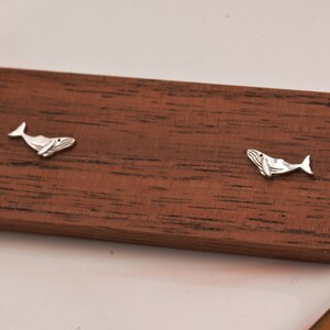 May include: A pair of silver whale earrings on a wooden surface.