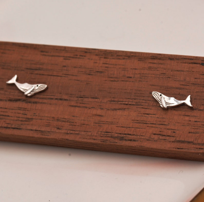 May include: A pair of silver whale earrings on a wooden surface.