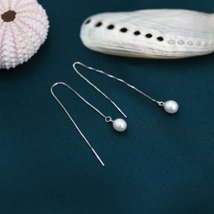 May include: A pair of silver chain earrings with a single white pearl dangling from each chain.