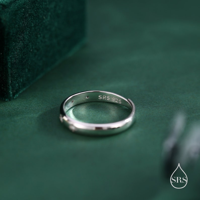 May include: A silver ring with a small diamond on the side. The ring is engraved with "SRS 925" on the inside.