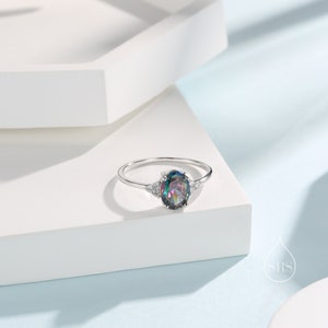 Puede incluir: Un anillo de plata con una gran piedra preciosa ovalada iridiscente rodeada de pequeñas piedras preciosas transparentes.