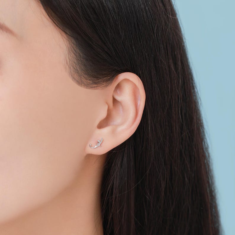 May include: A close-up of a person's ear with a small silver earring featuring a delicate leaf design.