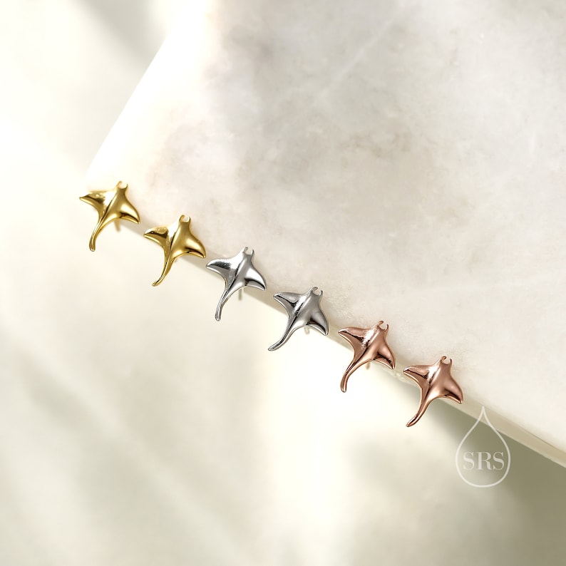 May include: Four pairs of sterling silver earrings in the shape of a manta ray. The earrings are shown in gold, silver, rose gold, and a darker silver finish.