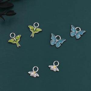 Puede incluir: Colección de abalorios plateados con forma de mariposas y polillas. Los abalorios presentan esmalte en tonos verdes y azules. Cada abalorio tiene un pequeño lazo para sujetarlo a joyas u otras manualidades.