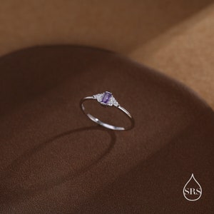 Puede incluir: Un delicado anillo de plata con una peque&ntilde;a piedra preciosa rectangular de color p&uacute;rpura rodeada de piedras preciosas m&aacute;s peque&ntilde;as de color claro.