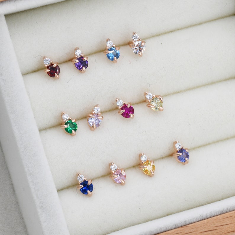 May include: A collection of 10 pairs of small stud earrings with a single gemstone and a small cluster of white stones. The gemstones are in various colors, including red, purple, blue, green, pink, and yellow.
