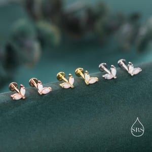 May include: An assortment of six ear piercing studs. The studs feature a three-petal design with a white opal-like stone. The metal colors include rose gold, gold, and silver. The earrings are displayed on a dark green velvet surface.