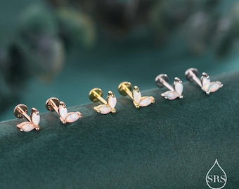 May include: An assortment of six ear piercing studs. The studs feature a three-petal design with a white opal-like stone. The metal colors include rose gold, gold, and silver. The earrings are displayed on a dark green velvet surface.
