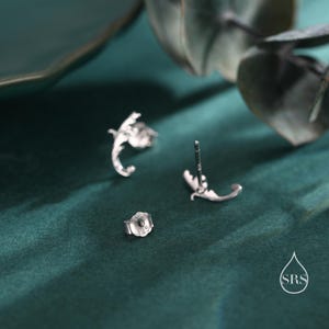 May include: A pair of silver earrings with a delicate floral design. The earrings are shown from the back, revealing the post and butterfly backing.