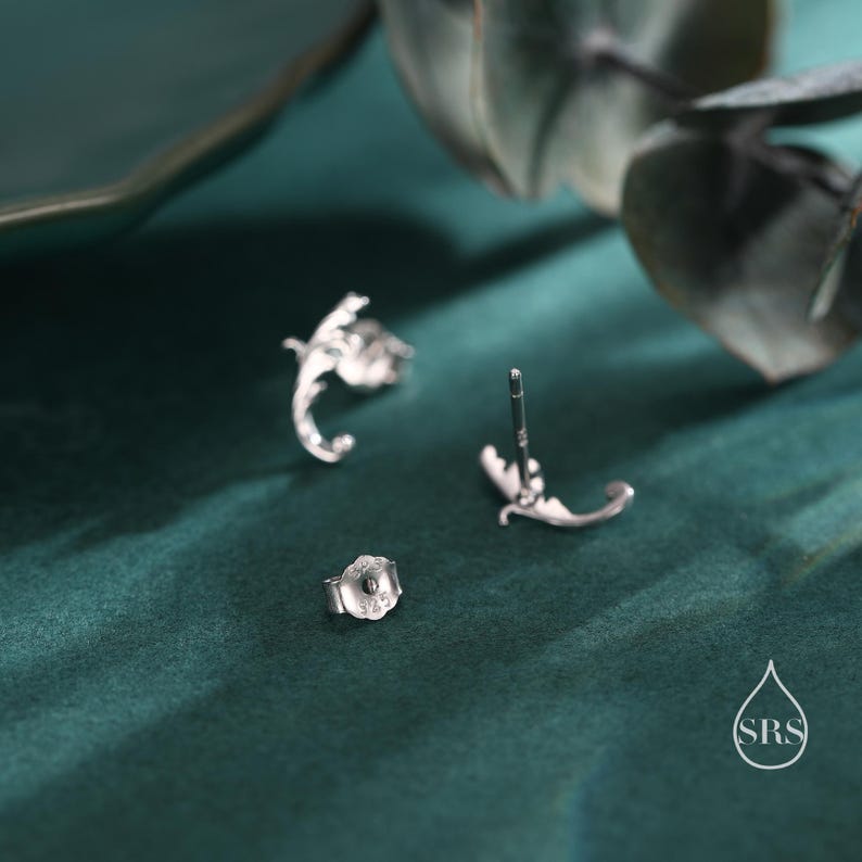 May include: A pair of silver earrings with a delicate floral design. The earrings are shown from the back, revealing the post and butterfly backing.