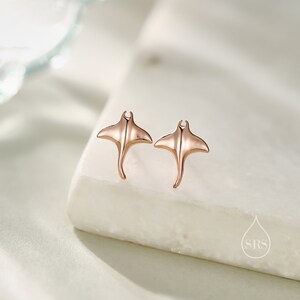 May include: A pair of rose gold stud earrings featuring a manta ray design.