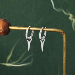 Op de afbeelding: Een paar zilveren oorringen met een puntige punt die aan elke ring hangt.