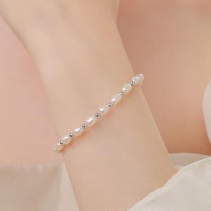 May include: A delicate pearl bracelet with small, white pearls and silver accents. The bracelet is on a person's wrist.