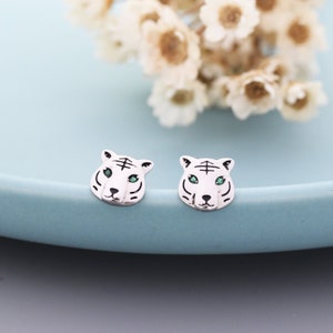 May include: A pair of silver tiger head stud earrings with green gemstone eyes.