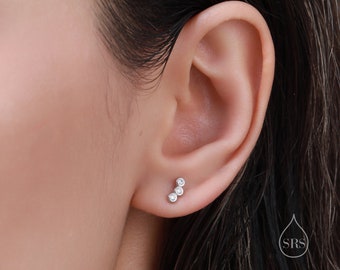 Puede incluir: Primer plano de una oreja con un pequeño pendiente de plata con tres piedras redondas transparentes dispuestas en línea curva.