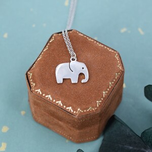 May include: A silver elephant charm necklace in a brown velvet box. The necklace has a delicate chain and a simple elephant pendant.